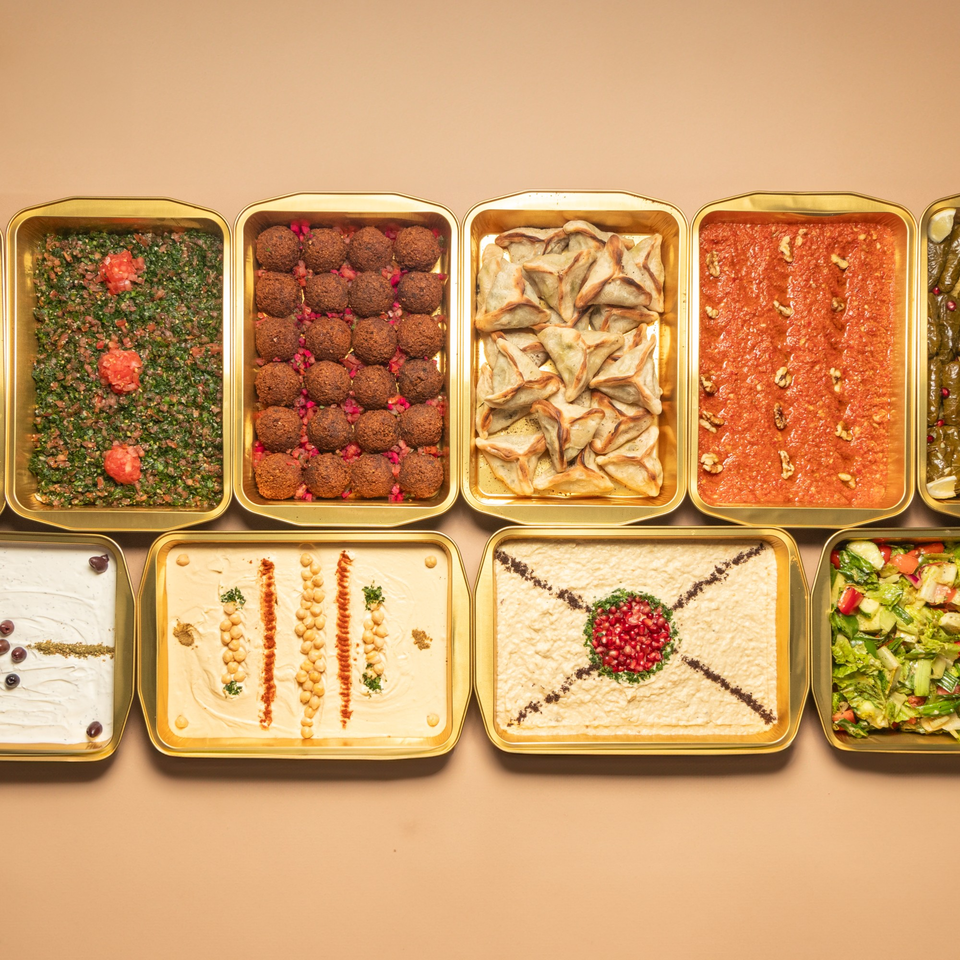 Top-down view of golden trays filled with various Lebanese dishes like tabbouleh, falafel, and hummus.