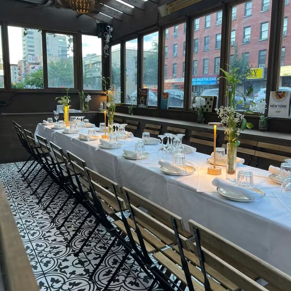 Long dining table set for guests with white tablecloth, glasses, plates, and floral centerpieces at Balade.
