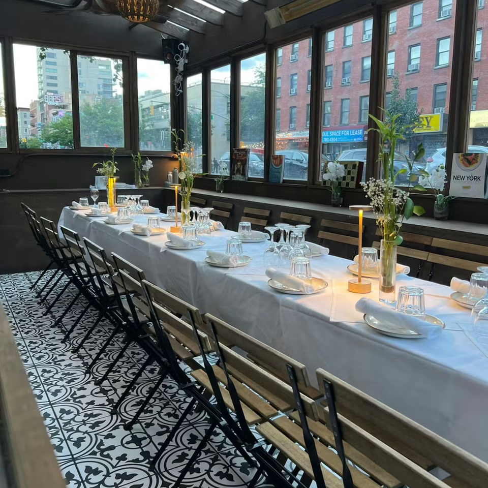 Long dining table set for guests with white tablecloth, glasses, plates, and floral centerpieces at Balade.