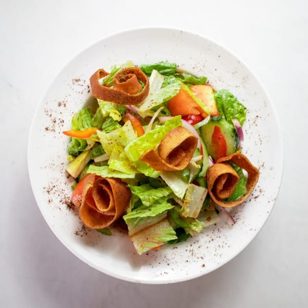 A vibrant Lebanese fattoush salad with fresh vegetables and crispy bread on a white plate.