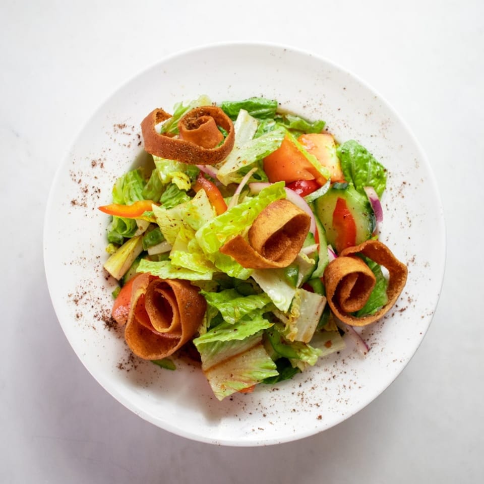 A vibrant Lebanese fattoush salad with fresh vegetables and crispy bread on a white plate.