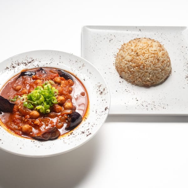 Lebanese dish with eggplant, chickpeas, and tomato sauce, garnished with scallions, served with rice.