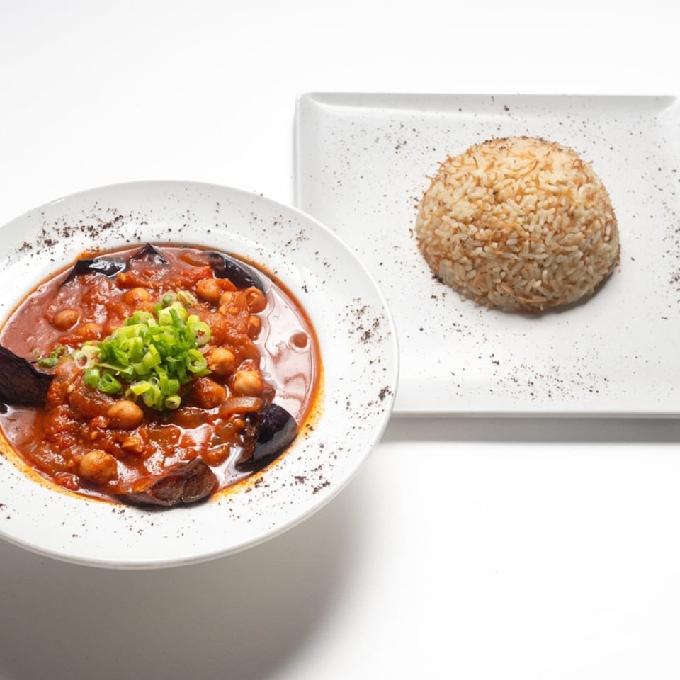 Lebanese dish with eggplant, chickpeas, and tomato sauce, garnished with scallions, served with rice.