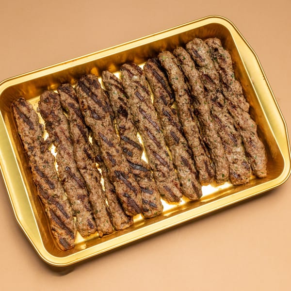 Grilled Lebanese kafta kebabs with char marks, arranged neatly on a golden rectangular tray.