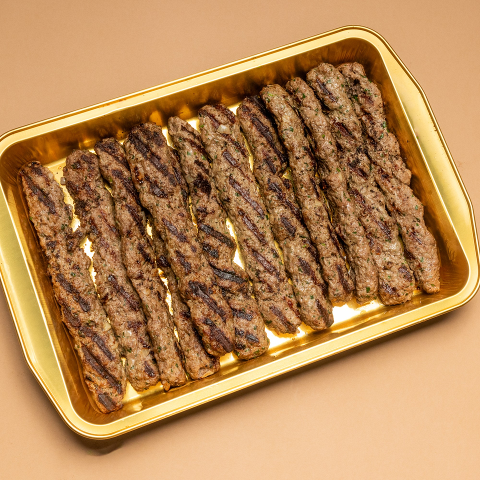 Grilled Lebanese kafta kebabs with char marks, arranged neatly on a golden rectangular tray.