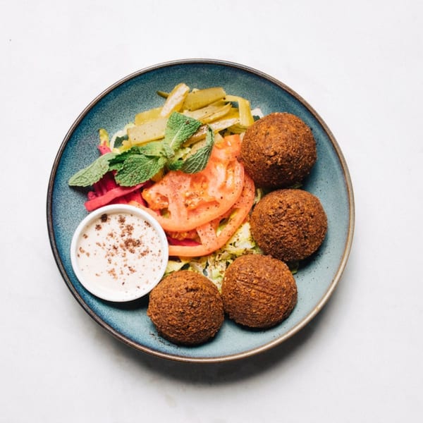 Four crispy falafel balls with sliced tomatoes, pickled vegetables, mint, and a dipping sauce.