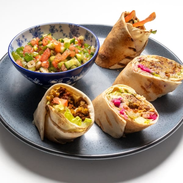 Four Lebanese shawarma wraps with various fillings, served with a side of chopped salad.