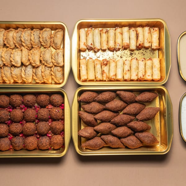 Four golden trays filled with various Lebanese appetizers, including sambousek, spring rolls, falafel, and kibbeh.