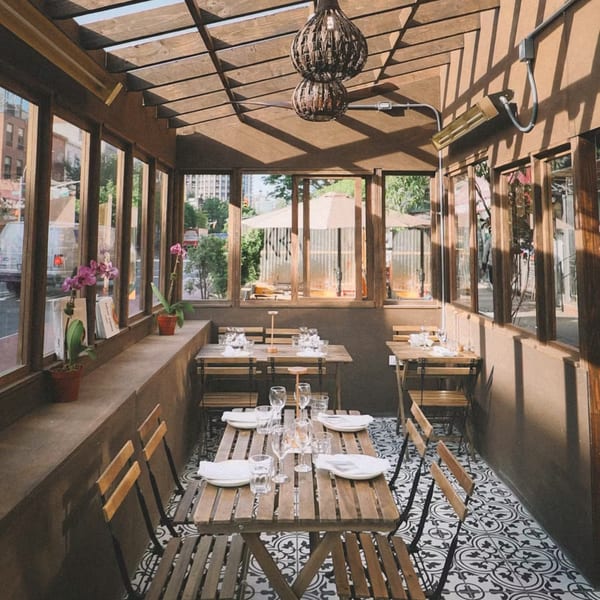 Sunlit Balade restaurant patio with wooden tables, chairs, and patterned floor tiles.