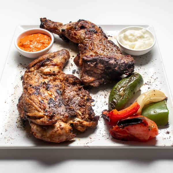 Grilled Lebanese chicken with roasted vegetables, red sauce, and white garlic dip on a white plate.