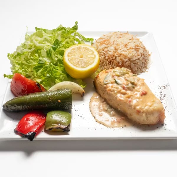 Lebanese chicken with creamy sauce, rice, grilled vegetables, lettuce, and lemon on a white plate.